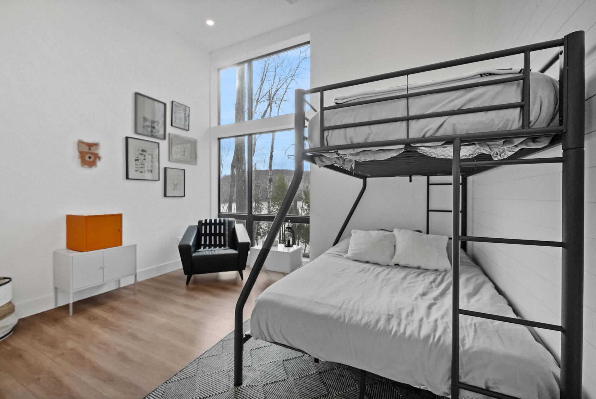 Bright bedroom with black bunk bed, white desk, wall art, and large window.