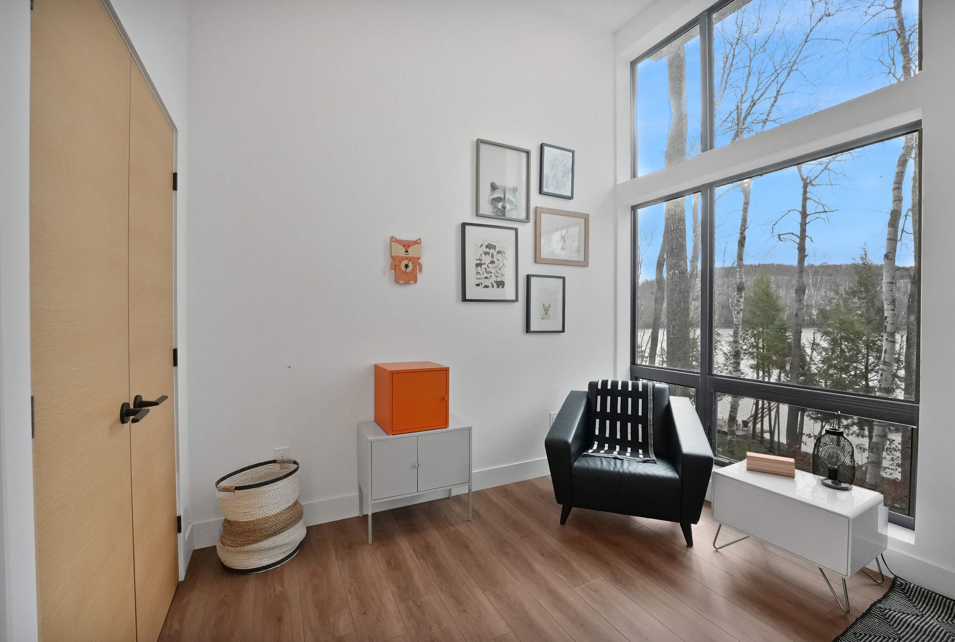Bright modern corner with chair, small tables, wall art, and large window overlooking trees