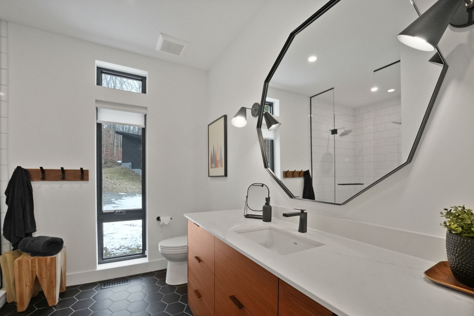 Modern bathroom with white walls, black floor tile, wood vanity, and large octagonal mirror