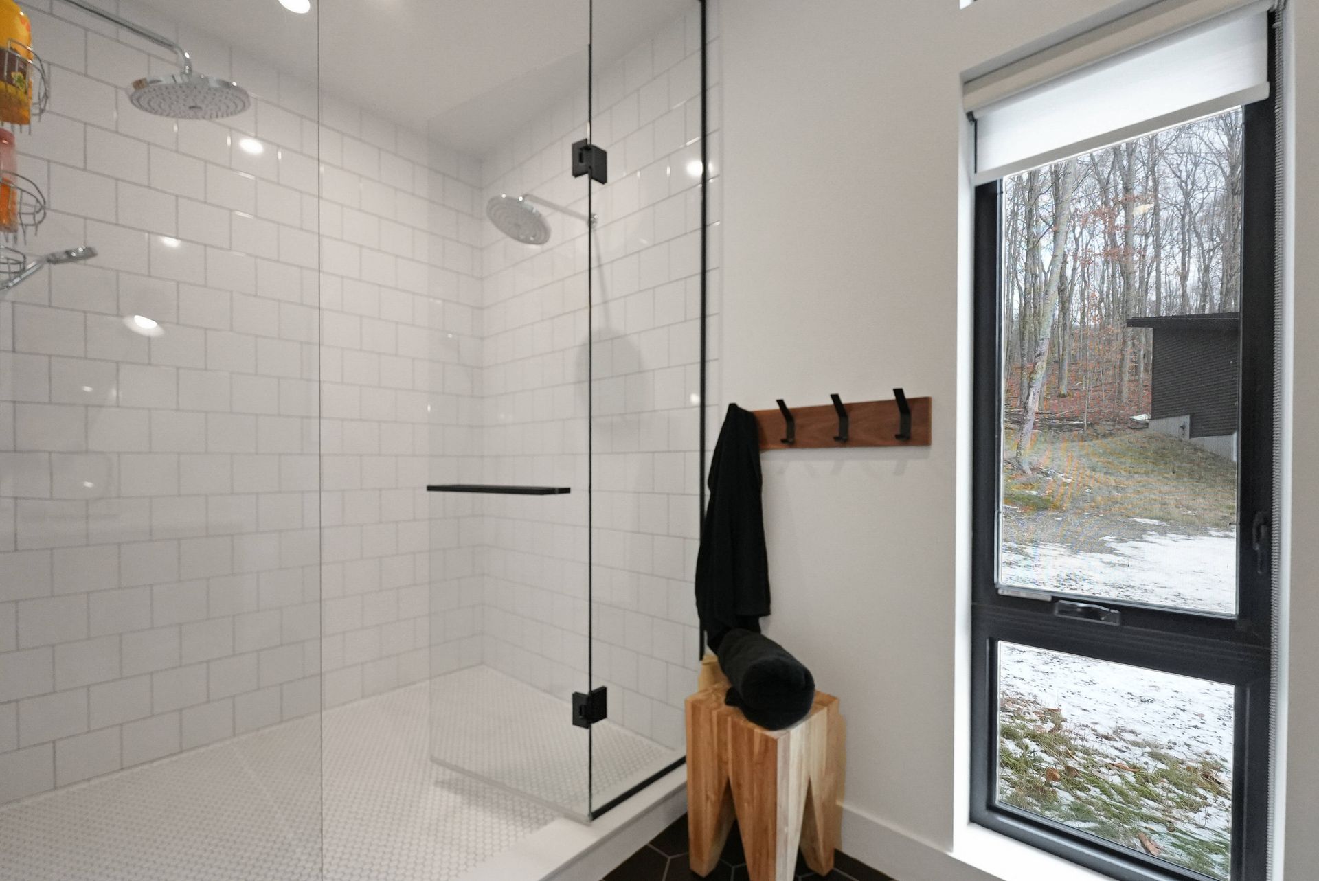 Modern bathroom with white tile shower, glass door, towel rack, and snowy window view