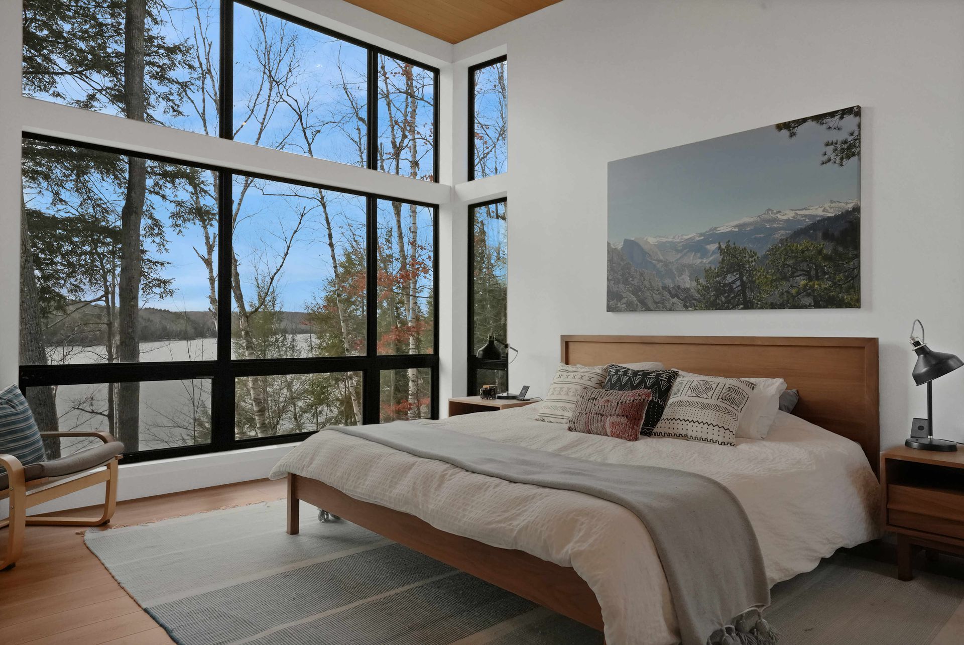 Modern bedroom with large windows, mountain view, wood bed, and a wall-mounted landscape photo