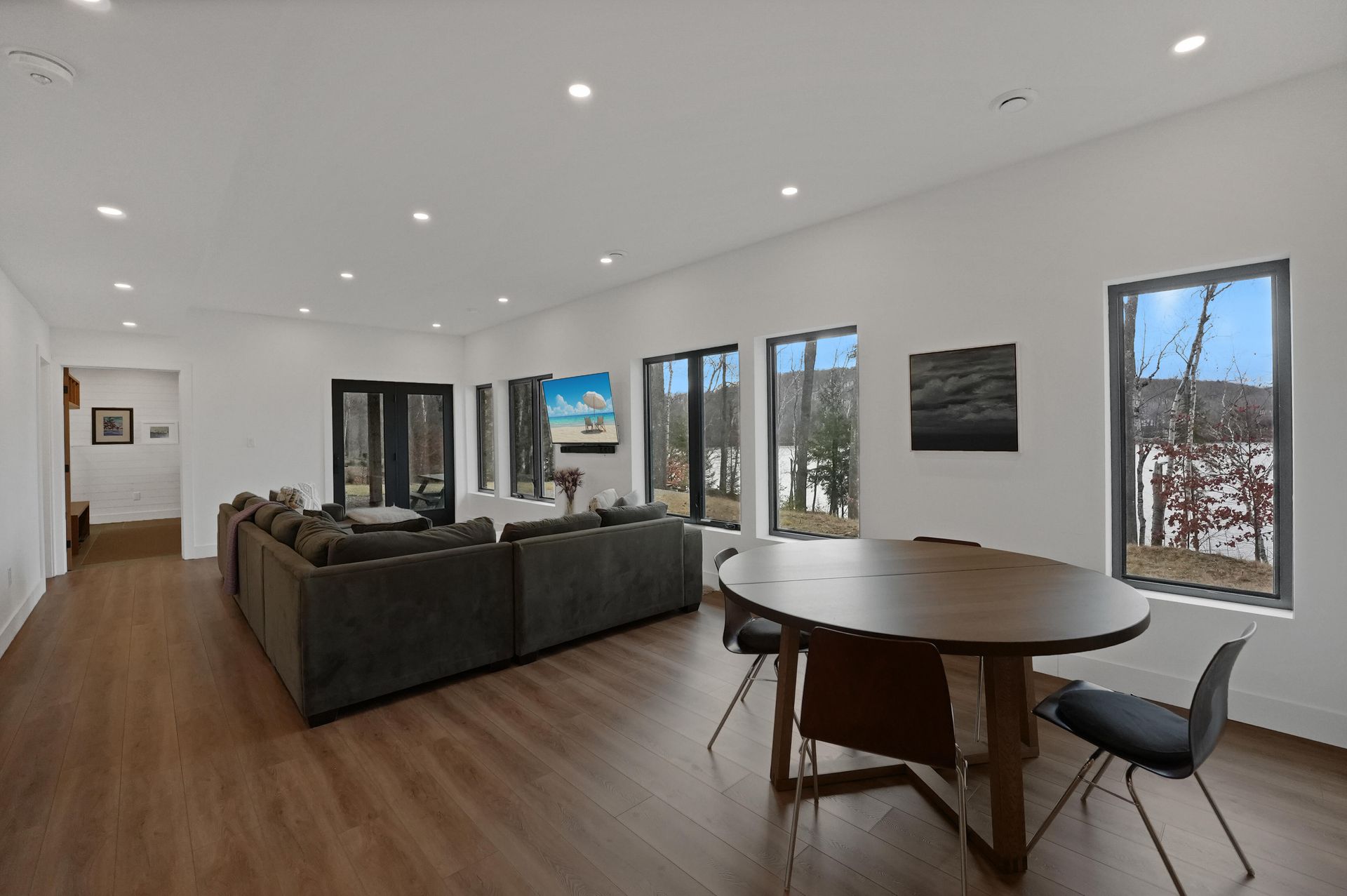 Bright modern living room with gray sofas, round table, wood floors, and large windows.