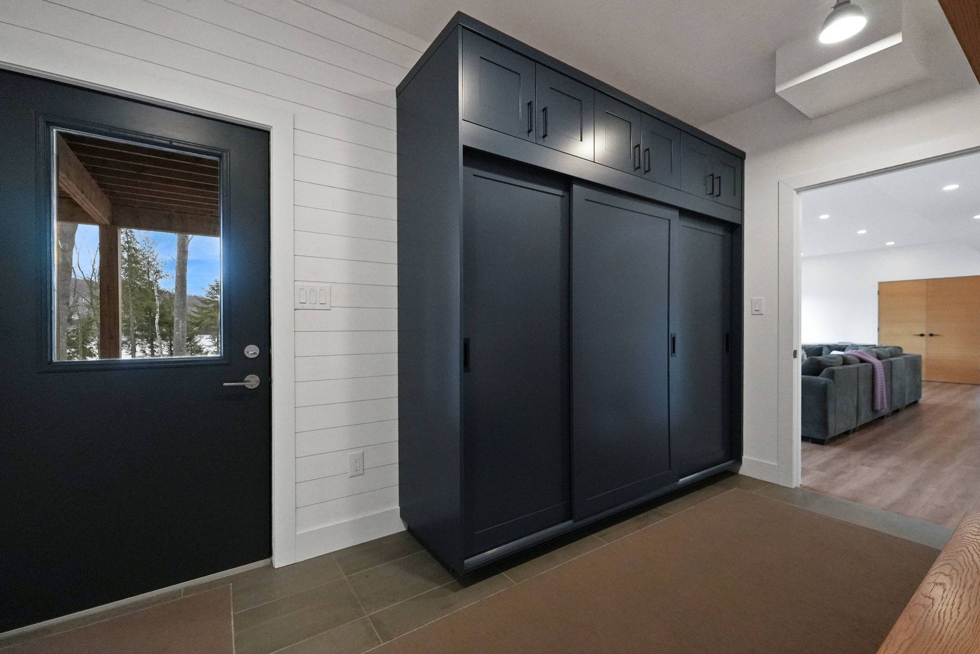 Modern entryway with black storage cabinets, a door, white brick wall, and tiled floor