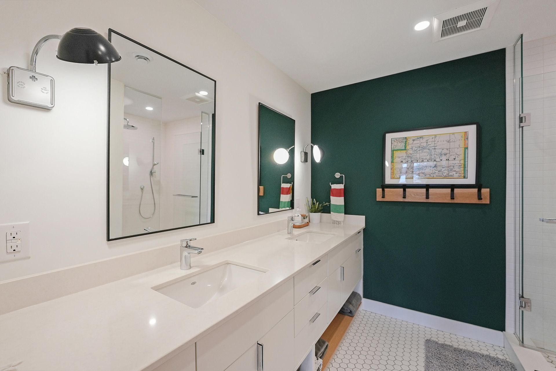Modern bathroom with long white vanity, mirrors, black sconces, and teal accent wall with towel hooks.