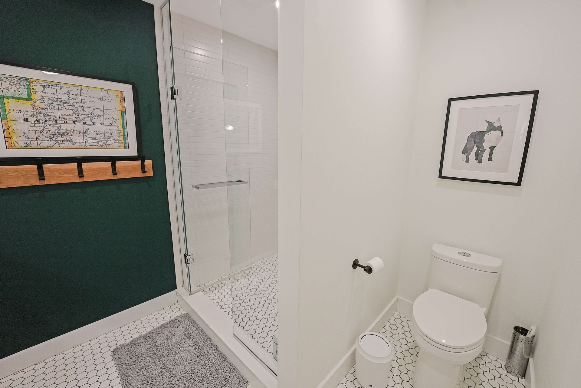 Modern bathroom with white toilet, glass shower, green accent wall, and framed wall art