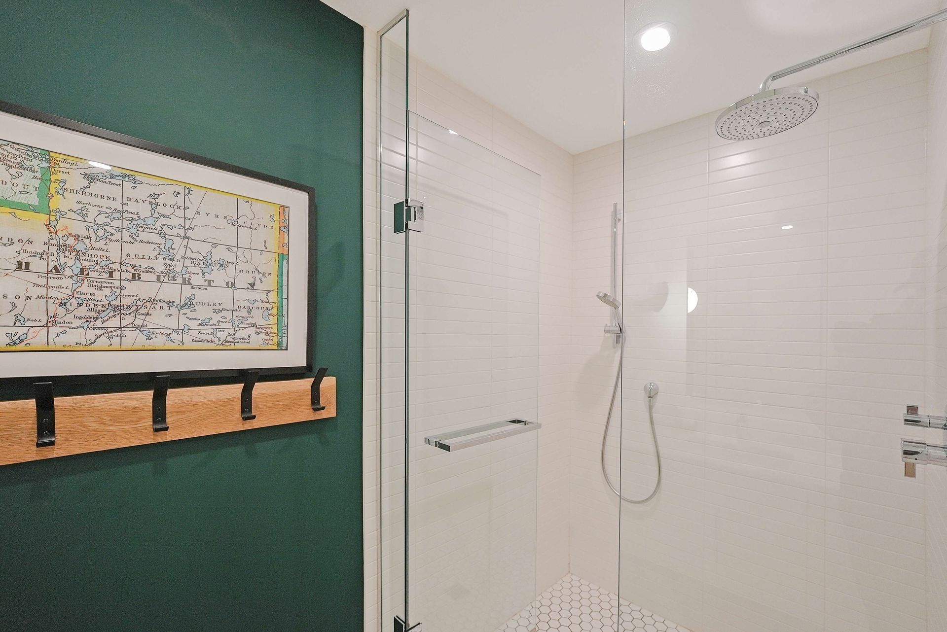 Modern bathroom shower with white tile, glass door, and green accent wall with a framed map.