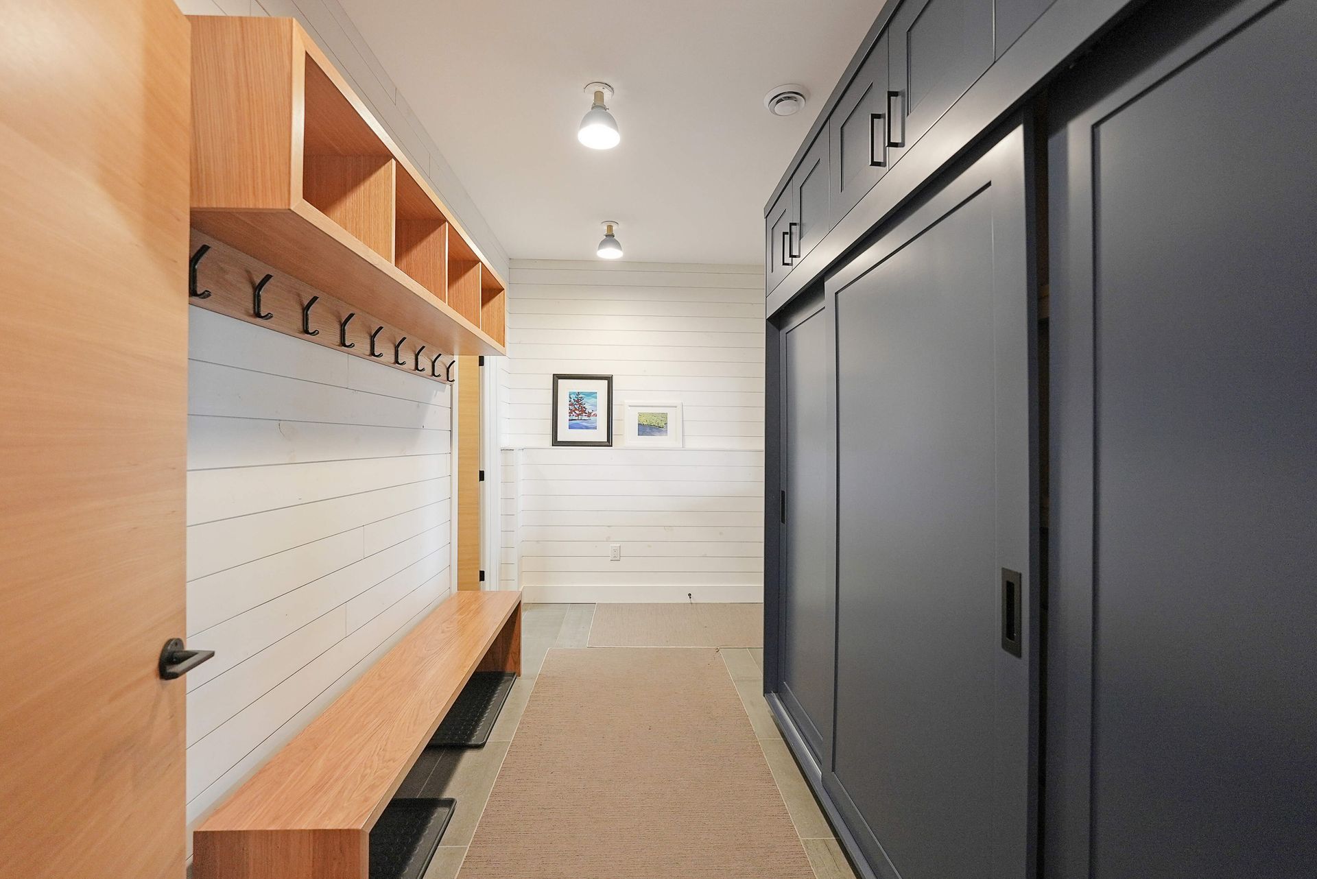 Modern mudroom with wood lockers, black cabinets, bench, and white shiplap walls