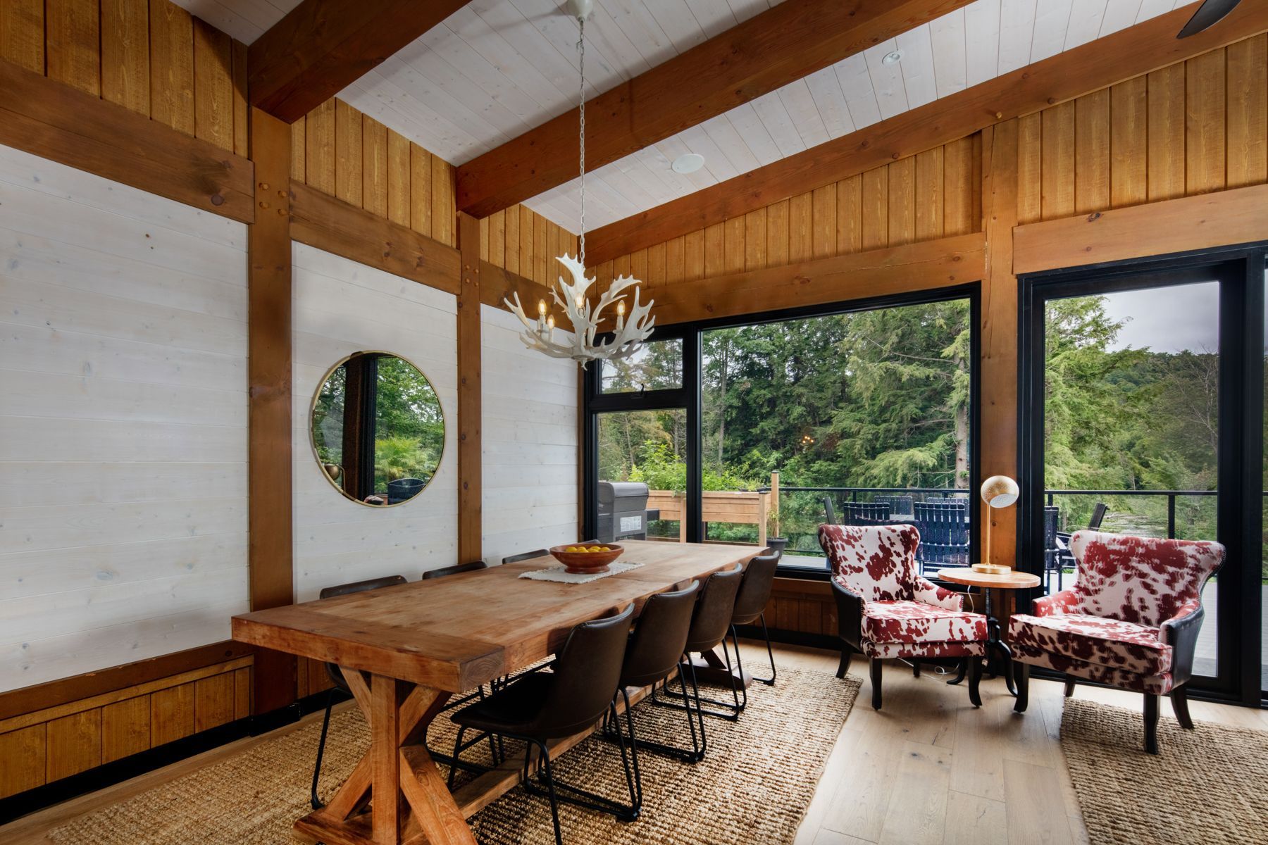 Modern dining room with wooden table, mixed chairs, large windows, and hanging light fixtures