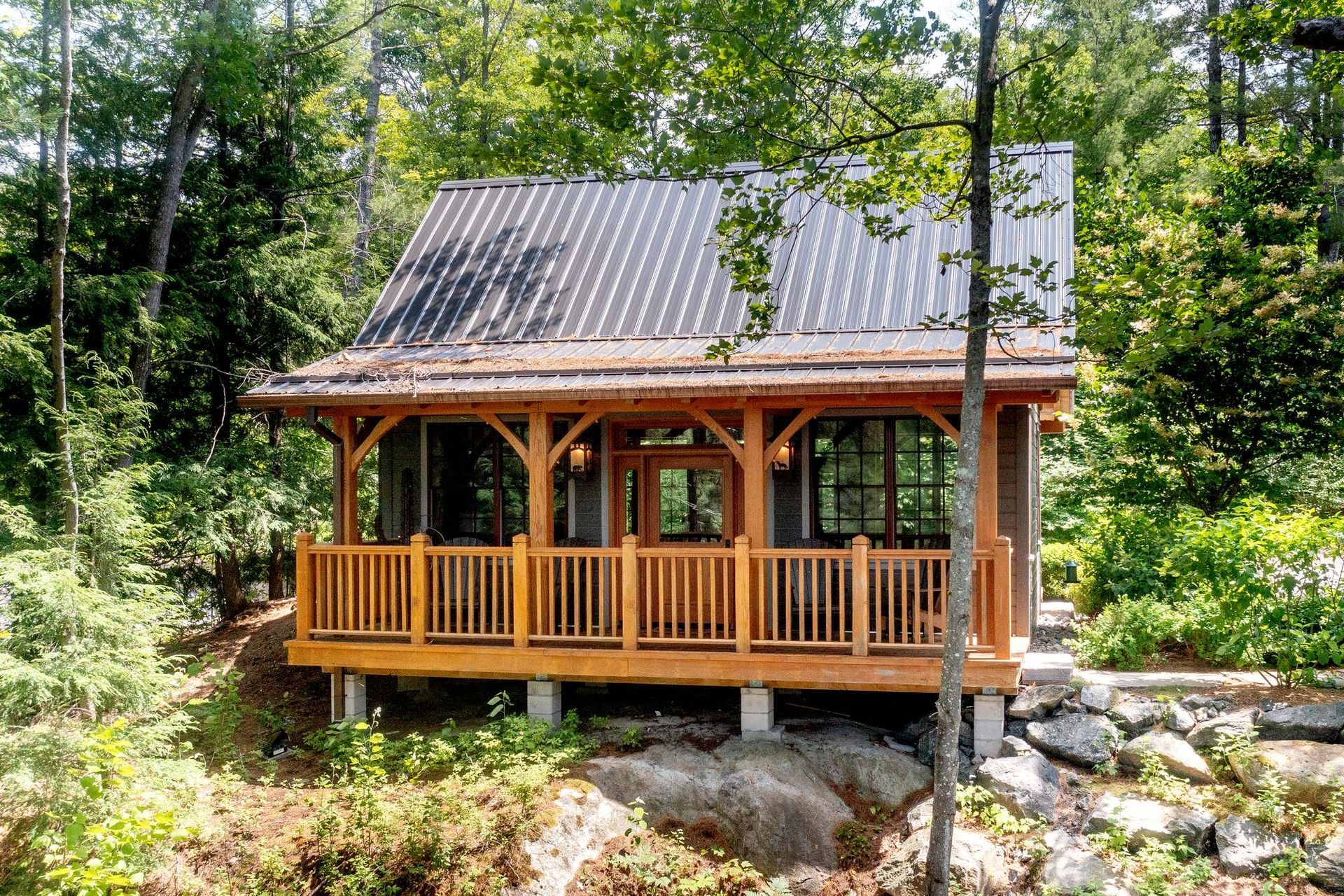 Wooden cabin with porch and metal roof nestled in a wooded forest setting