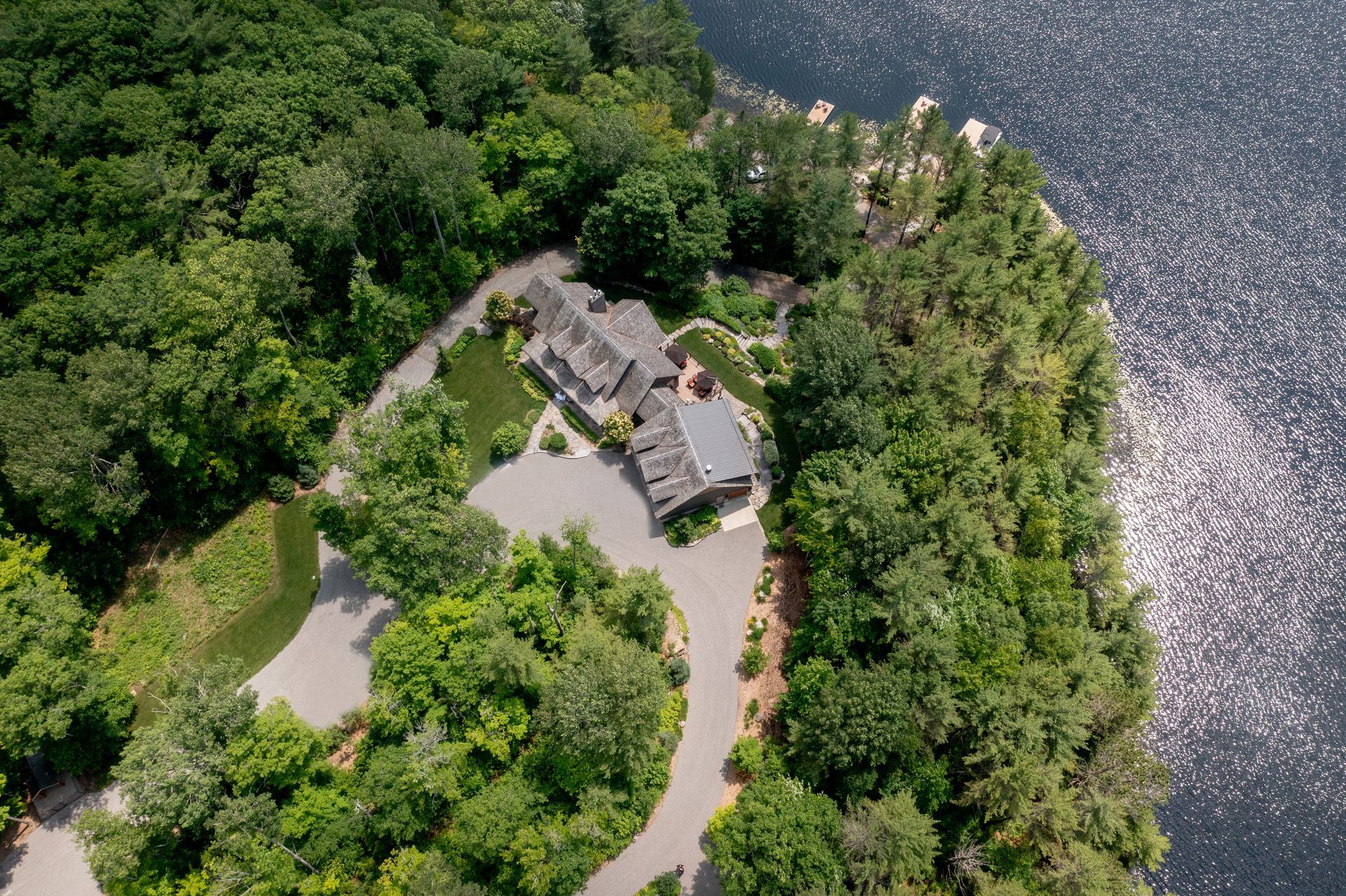 An aerial view of a house on a small island in the middle of a lake surrounded by trees.