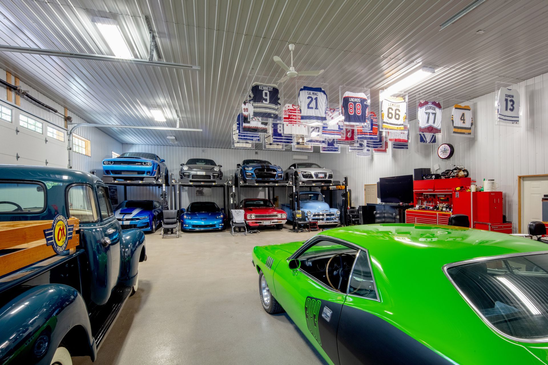 A garage filled with cars and trucks with jerseys hanging from the ceiling.