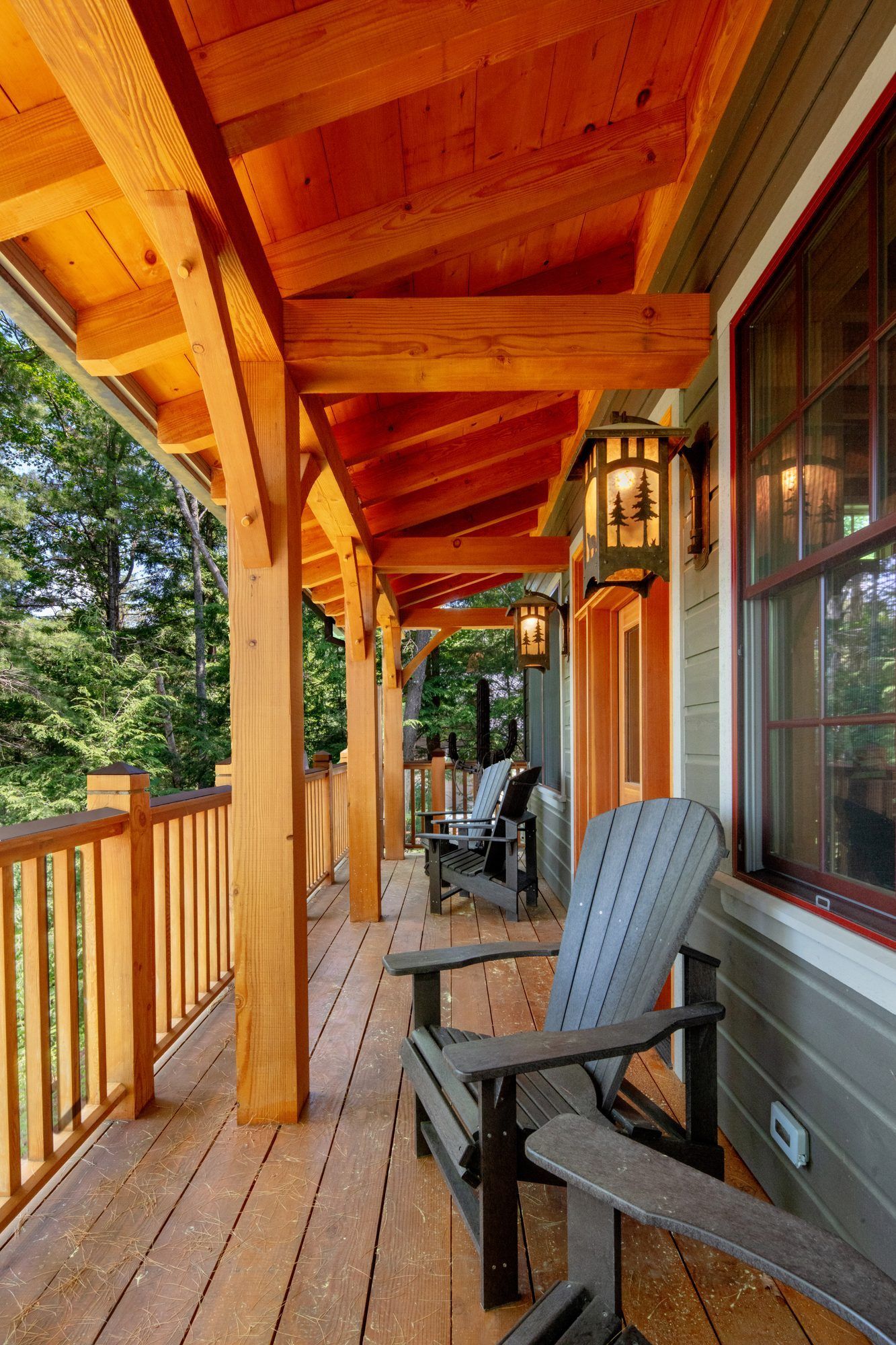 Wooden porch with log beams, chairs, and a railing beside large windows on a sunny day