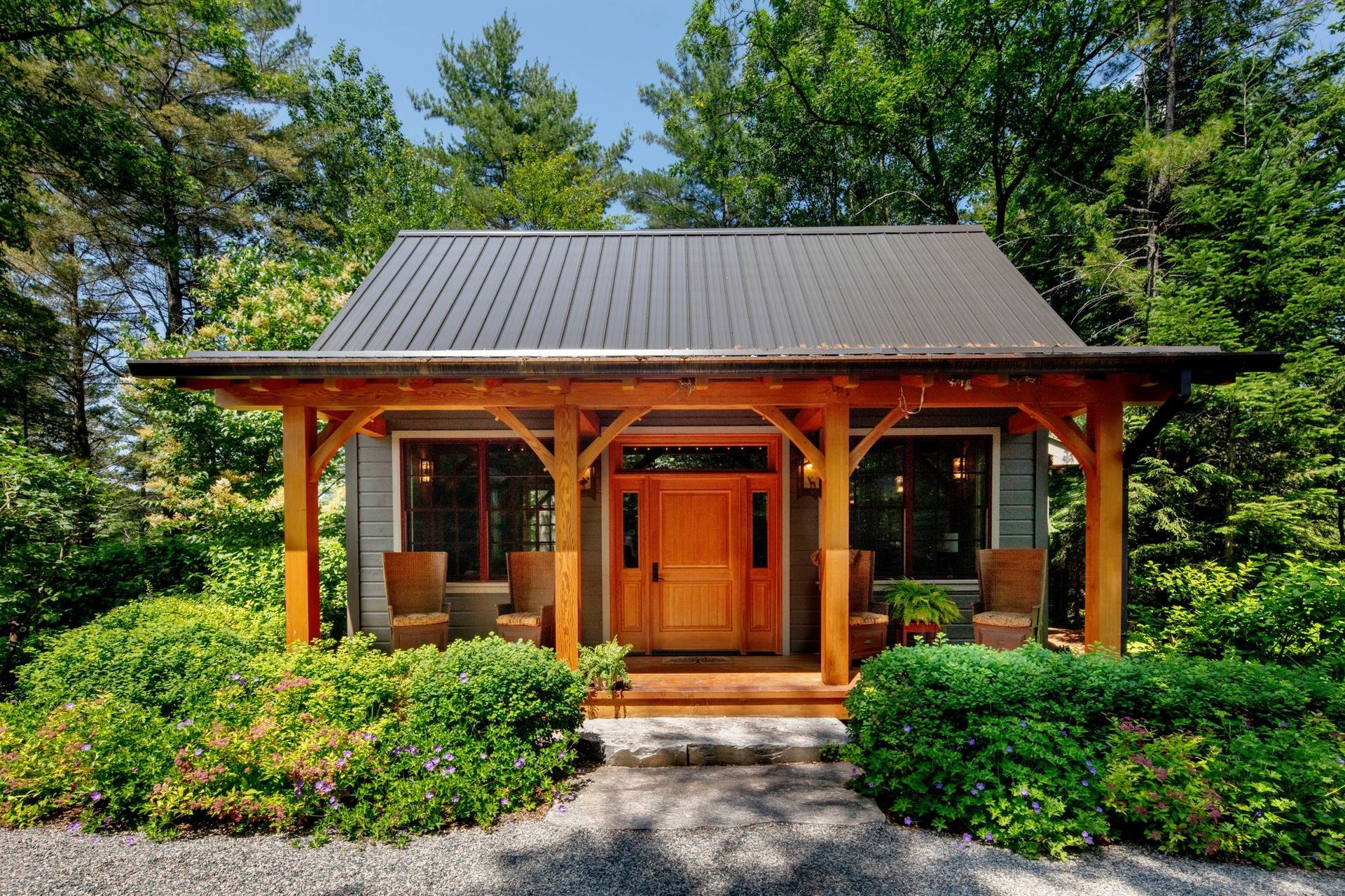 Wooden Japanese-style house with a porch, surrounded by lush green trees and shrubs