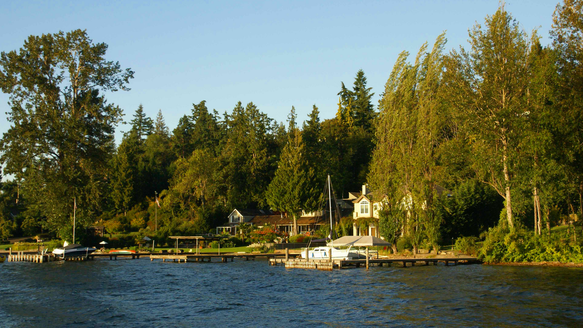 Calm lakeside scene with trees, docks, and a white boat under a clear blue sky