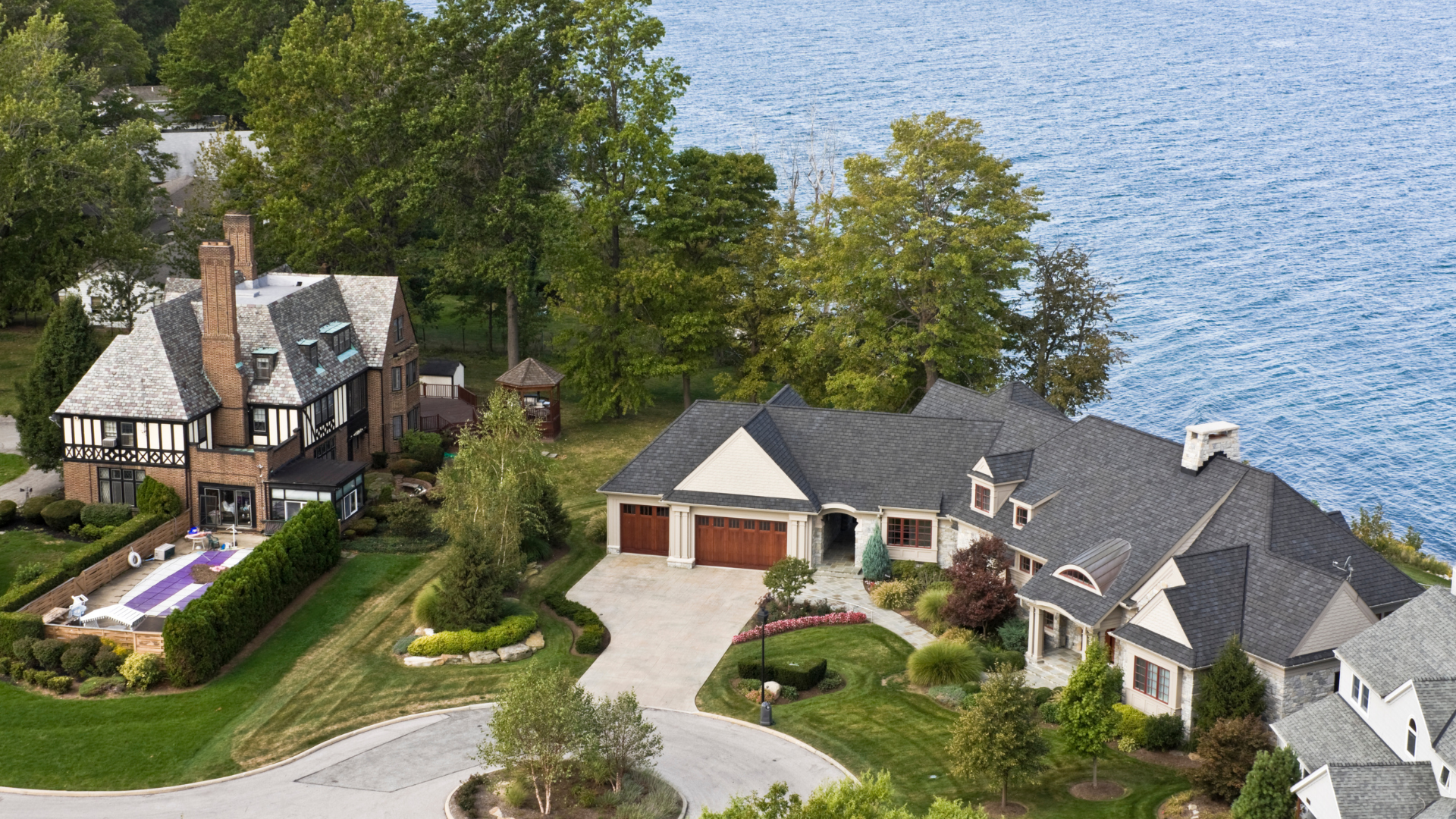 Two lakeside houses with docks, trees, and driveways along a calm shoreline