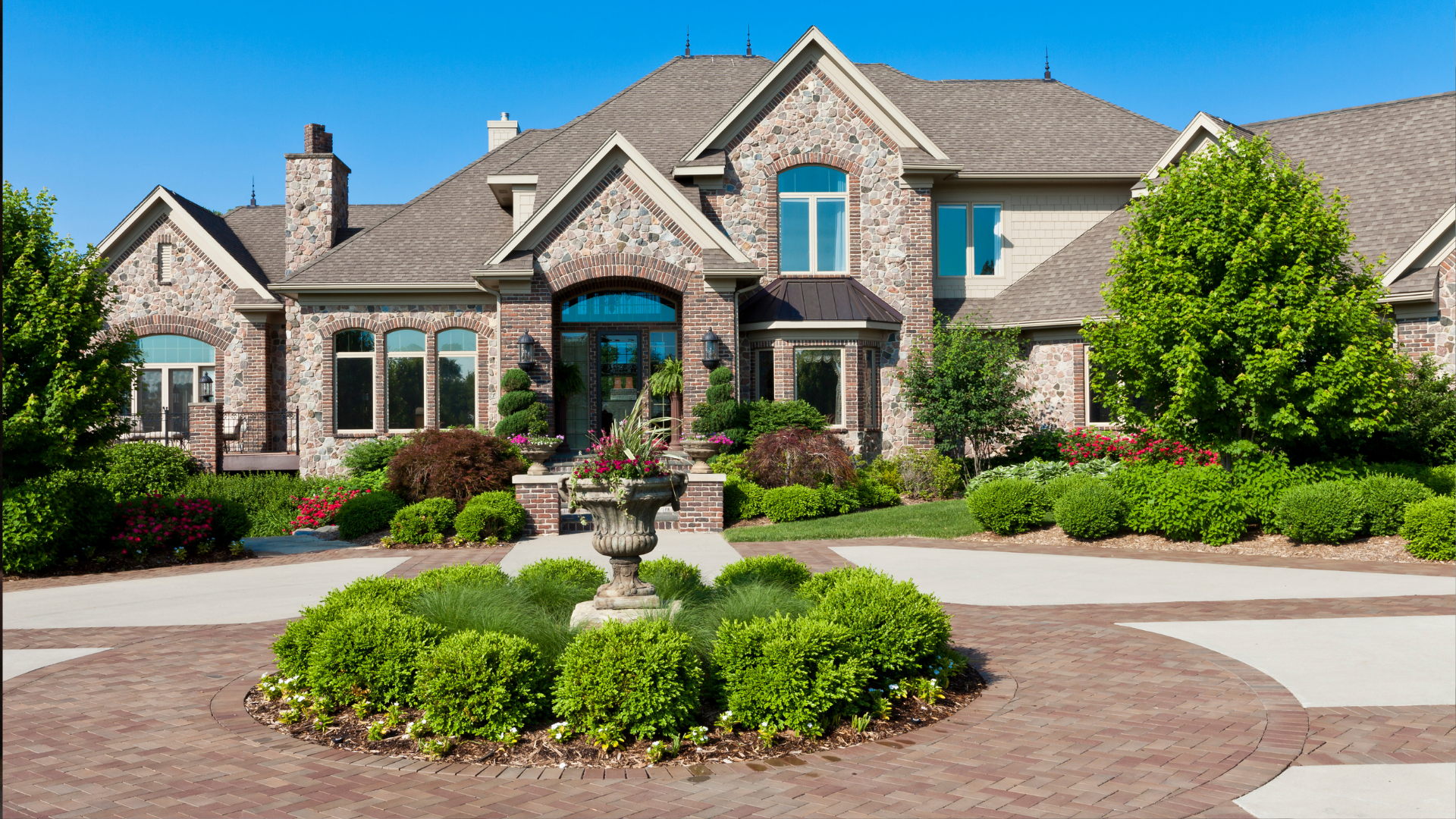 Luxury stone house with manicured landscaping, circular driveway, and central fountain