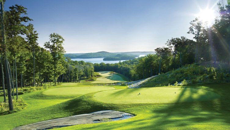 The sun is shining through the trees on a golf course with a lake in the background.