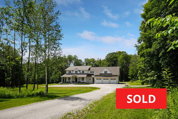 Modern two-story house with deck and gravel driveway, marked with a red “SOLD” sign.