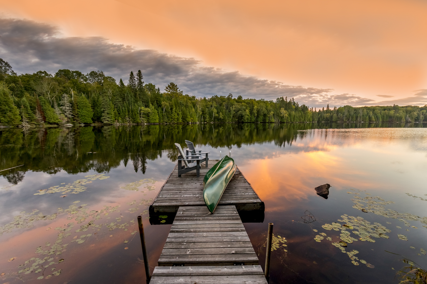 A canoe is sitting on a dock next to a lake at sunset.