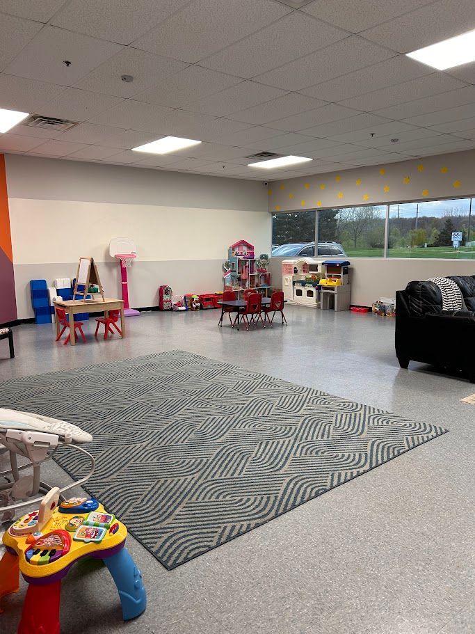 Children’s playroom with toys, small tables, and a gray patterned rug in a bright open space