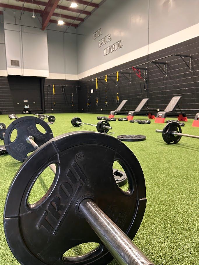 Barbell on turf in a gym, with weight plates and fitness equipment in the background