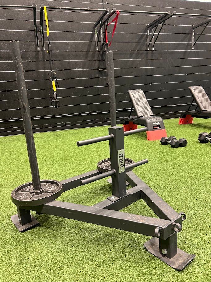 Prowler sled workout machine on turf in a gym, with weight plates and handles.