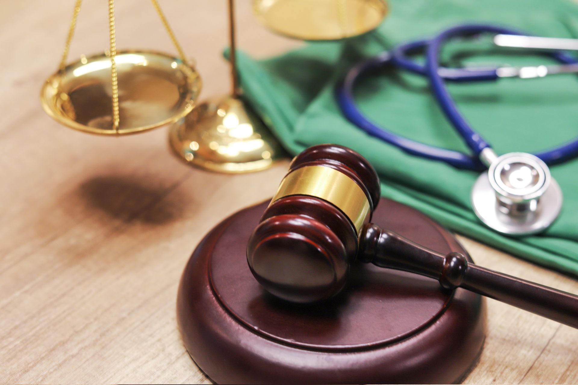 Scales of justice, gavel, stethoscope, and green scrubs representing medical legal issues.