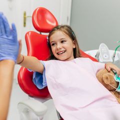 A little girl is sitting in a dental chair with a teddy bear.
