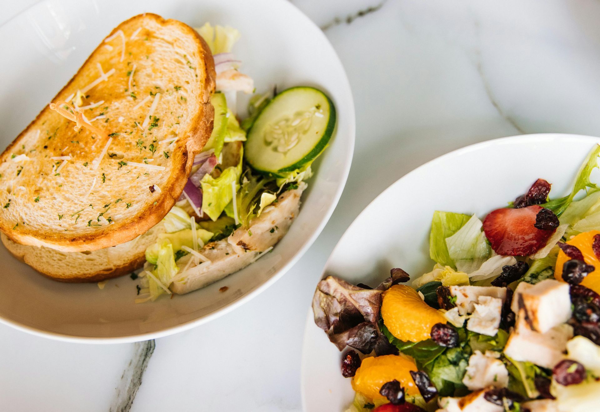 Sandwich and salad on white dinner plates on marble counter