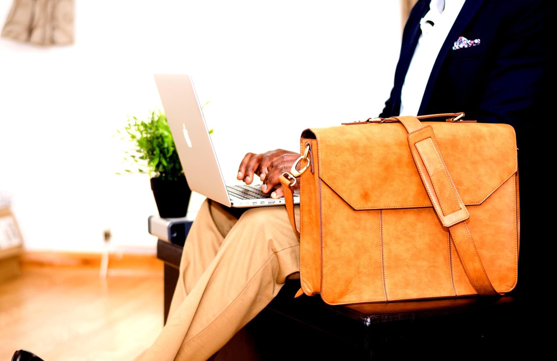 A man is sitting in a chair using a laptop and a briefcase