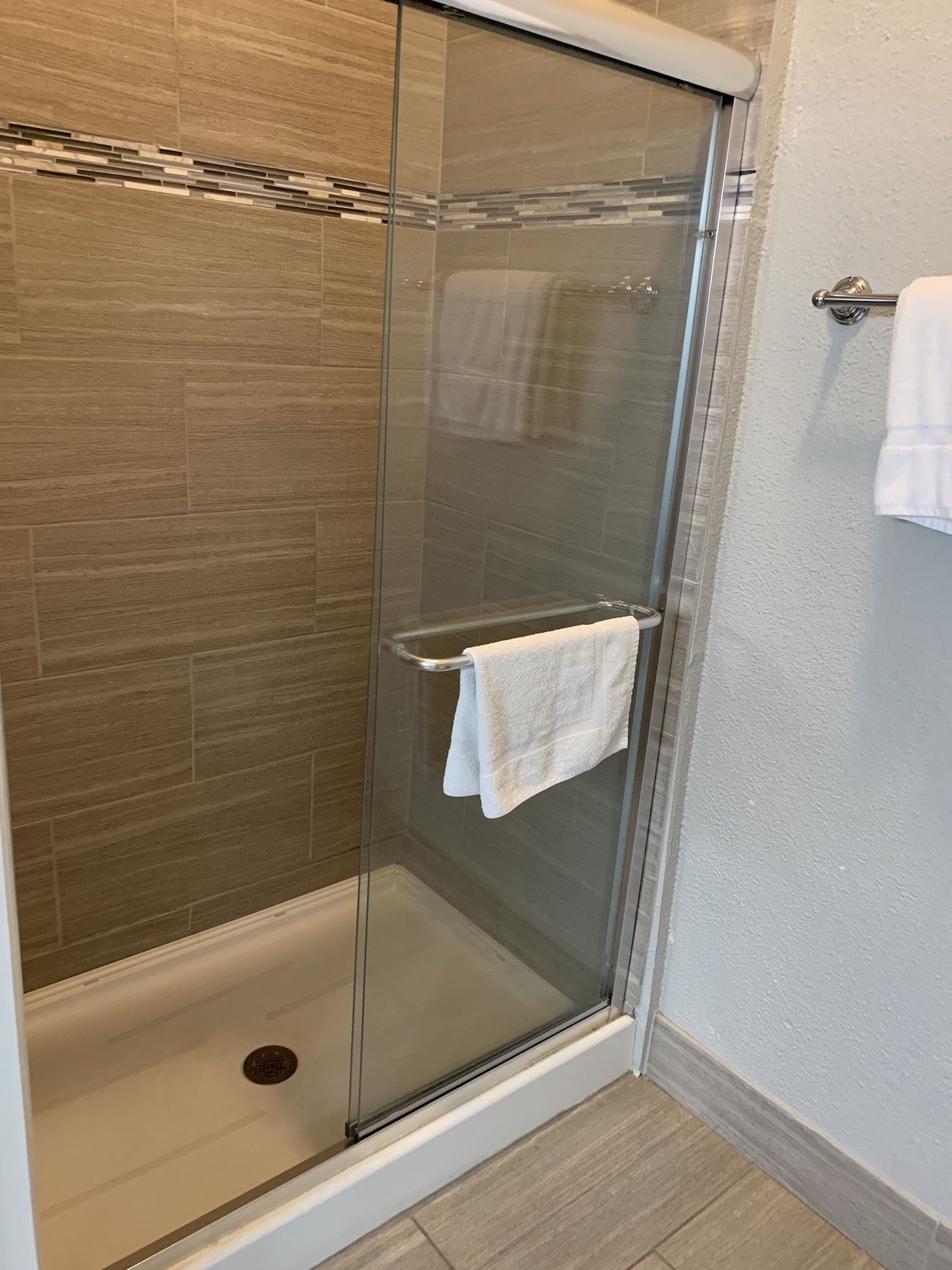 A bathroom with a walk in shower and a towel hanging on the door.