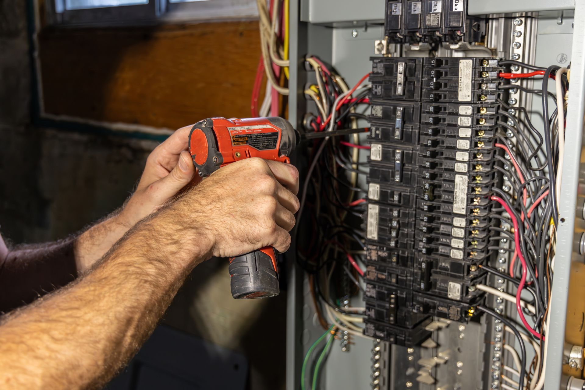 Person using a power tool on an electrical panel with wires; indoor setting. Person using a power tool on an electrical panel with wires; indoor setting.