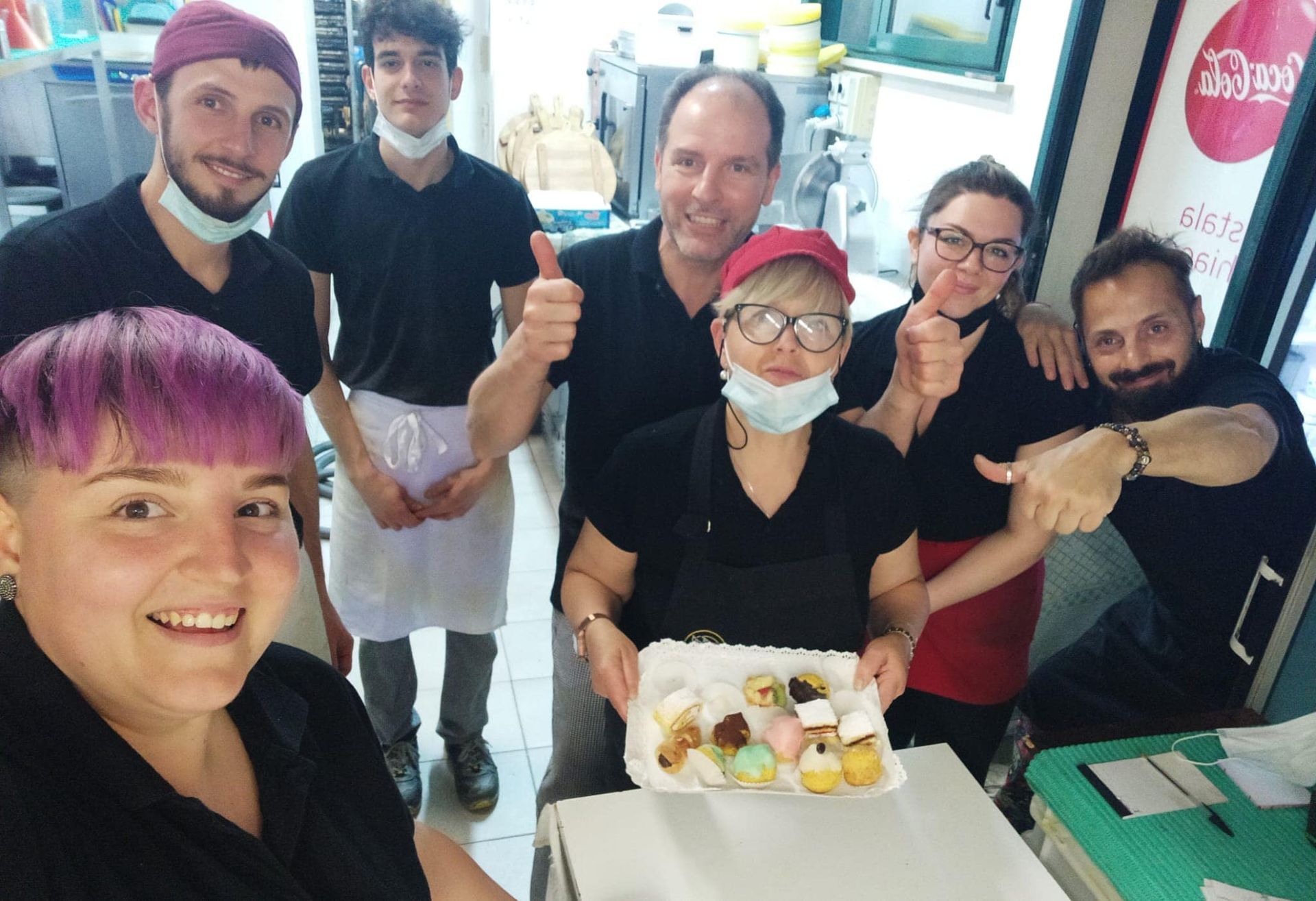 Due persone posano davanti alla Pizzeria Maria Regina, tenendo in mano una scatola di pizza davanti alla vetrina.