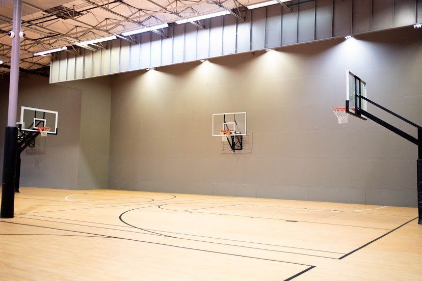 Indoor basketball court with three hoops against a grey wall and hardwood floor.