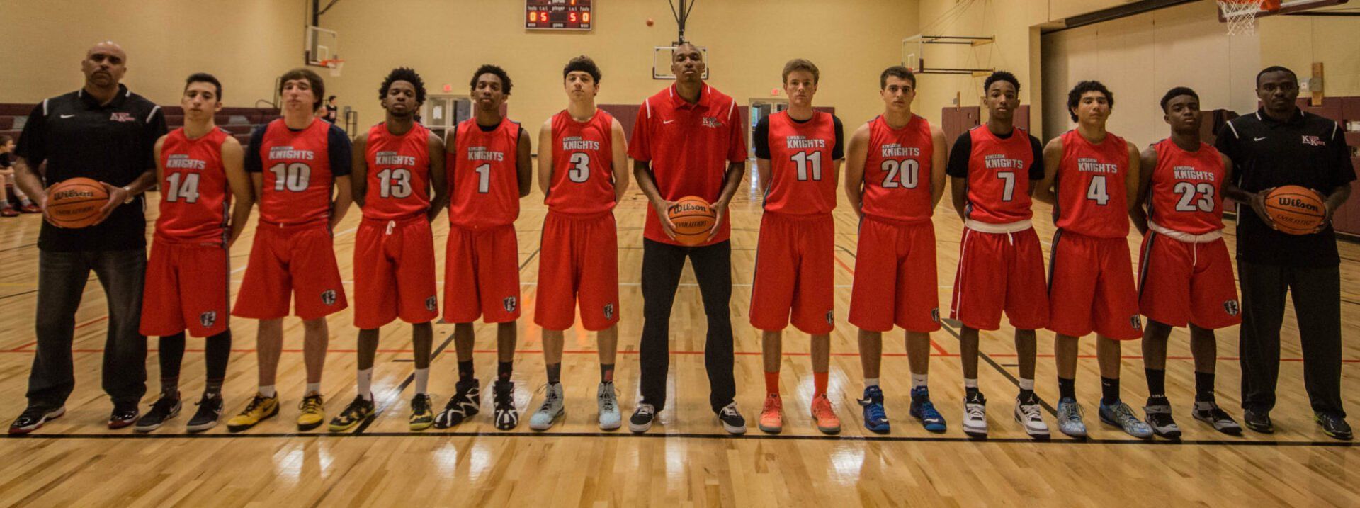 Basketball team in red jerseys and coaches, posed in a gym.