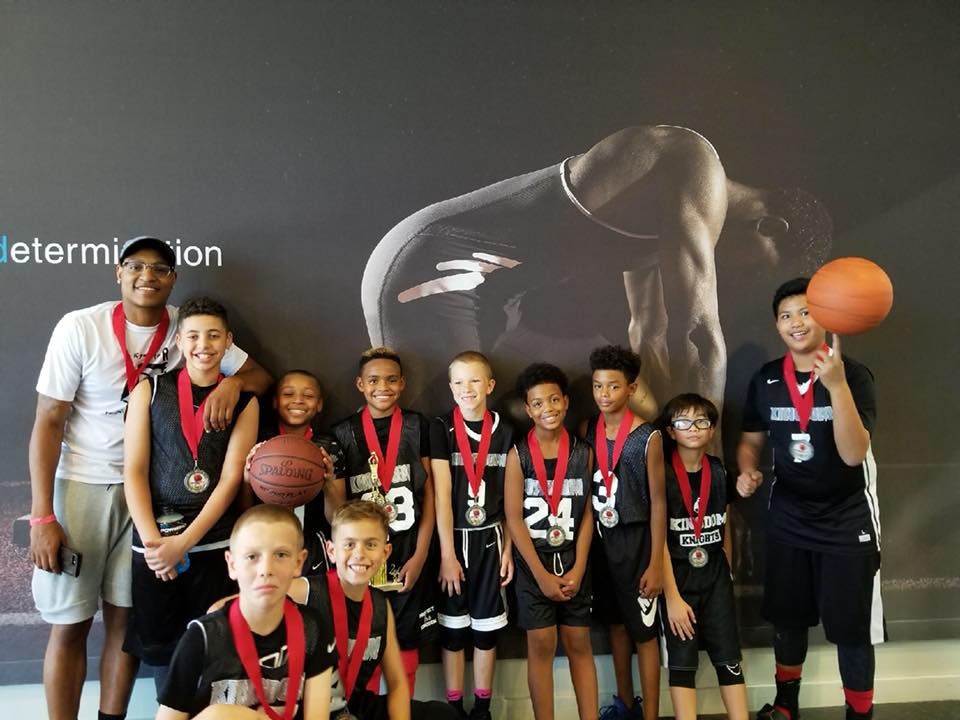 Youth basketball team with medals poses in front of a graphic, some holding basketballs.