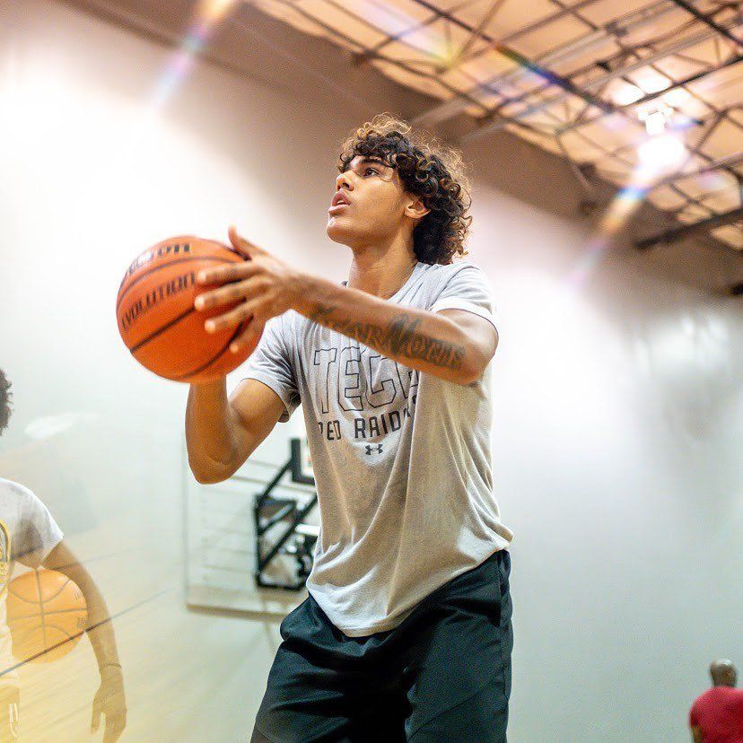 Basketball player in gray shirt shoots a ball in an indoor gym.