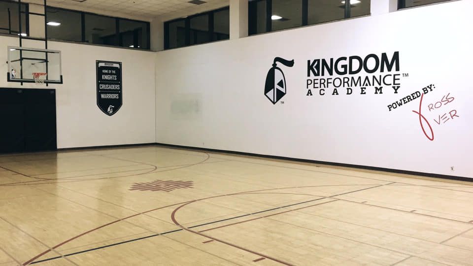 Basketball court with white walls, logo and hoop. Wooden floor.