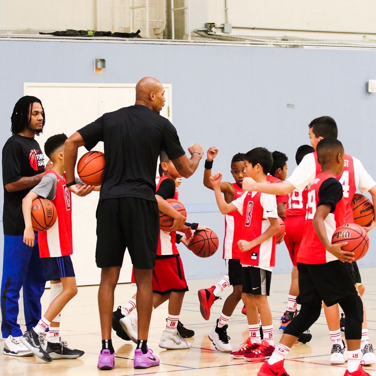 Basketball coaches and children in red uniforms high-five during practice. Court indoors.