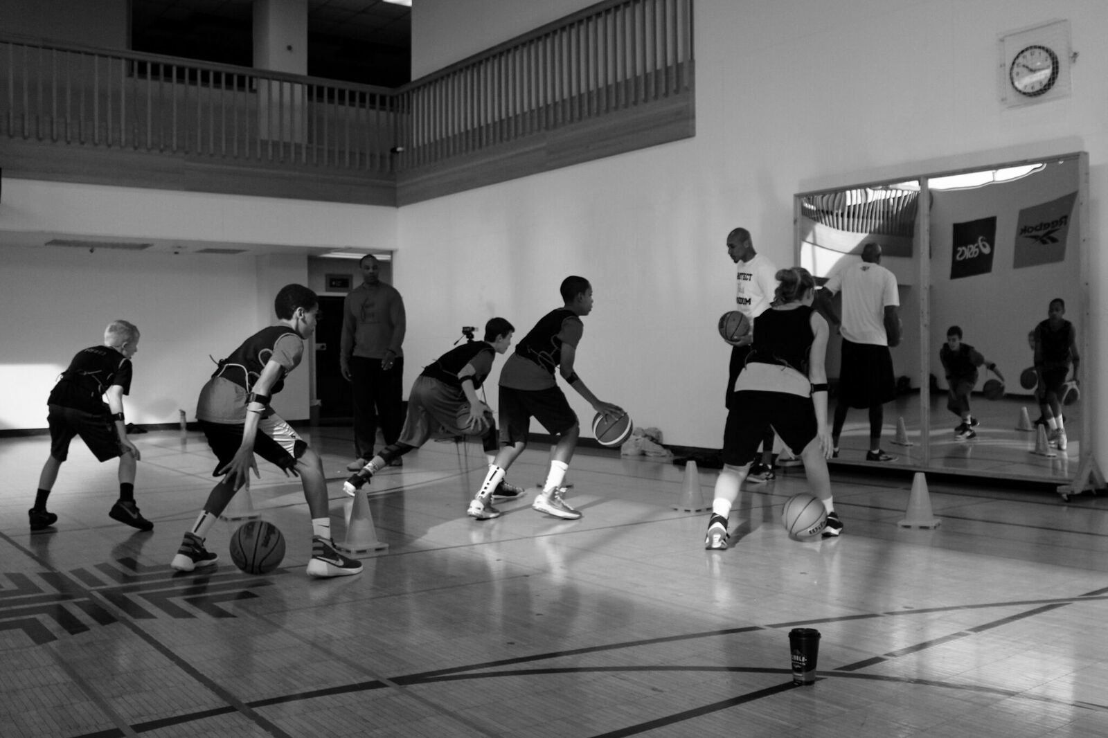 Basketball players practice dribbling in a gym with mirrors.