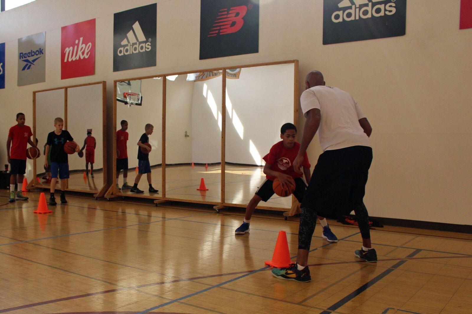 Basketball coach instructing a young player on dribbling technique in a gym. Other players watch.