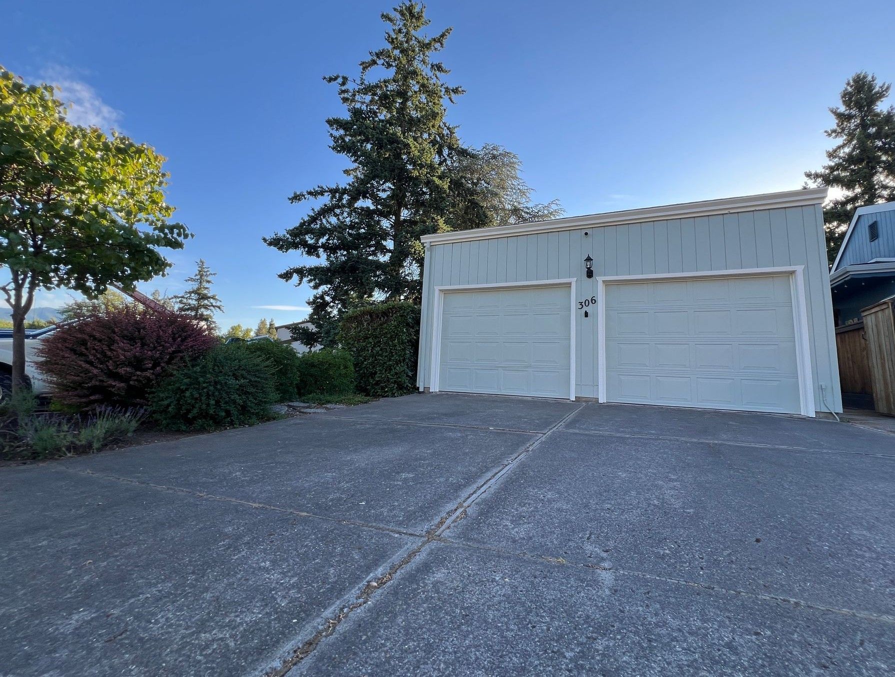 A two-car garage with light-blue siding, a dark roof, and a paved driveway, set against a clear blue sky.