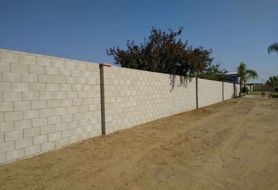 Long beige cinderblock wall beside a dirt road under a clear blue sky