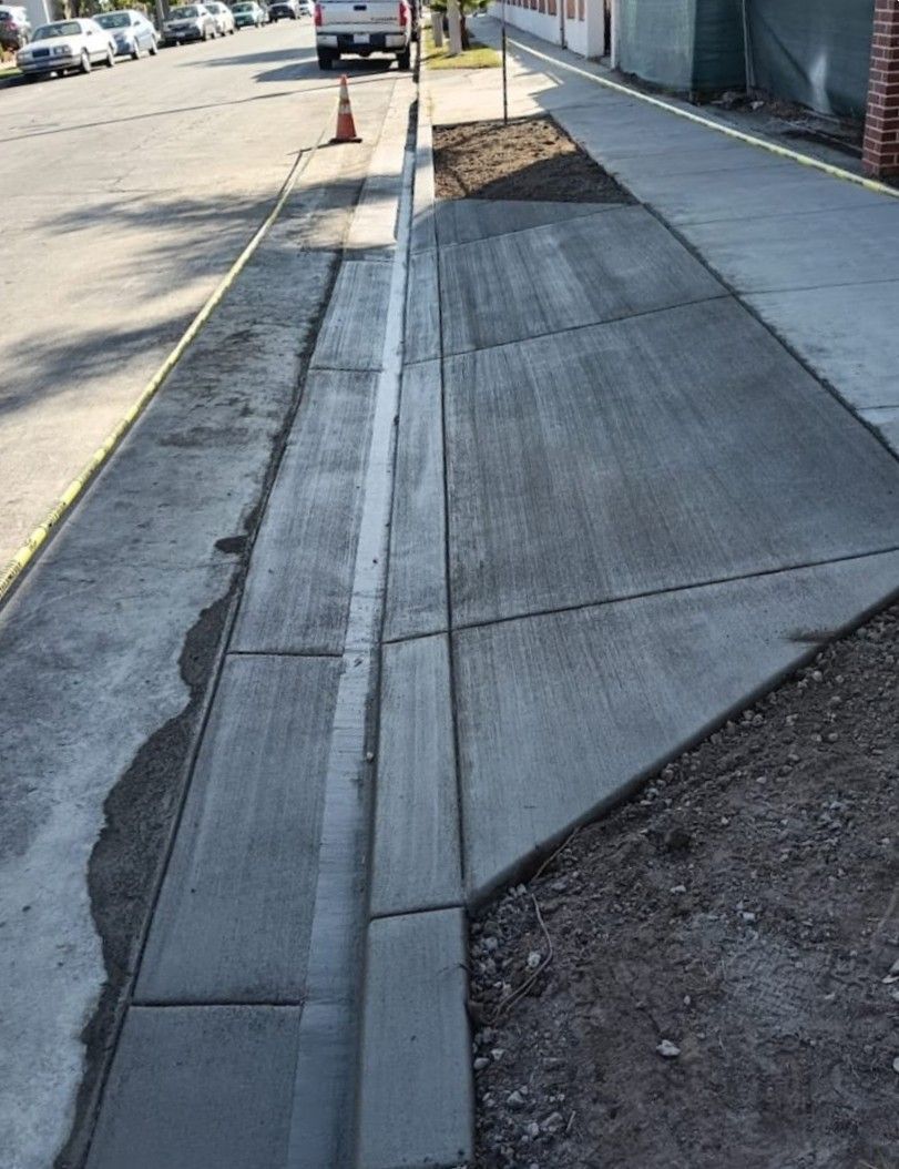 Sidewalk with a narrow curb ramp and tactile strip beside a street and parked cars