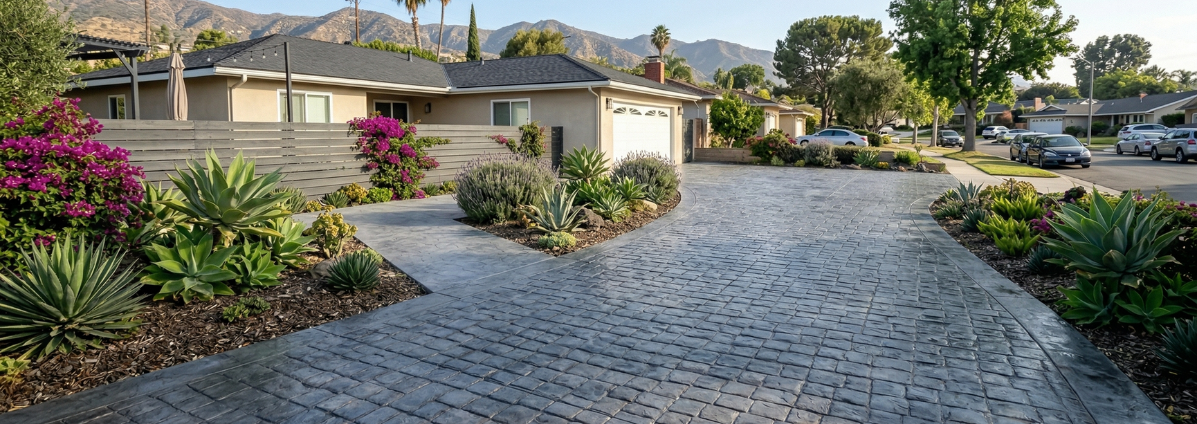 Residential driveway with gray pavers, landscaped flower beds, and houses in the background