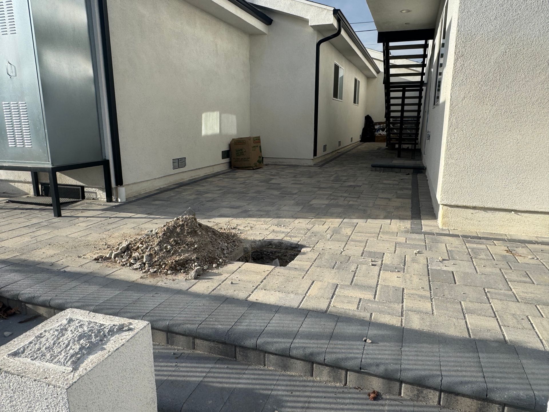 Outdoor walkway beside a building, with paving stones, stairs, and a small pile of debris in the path