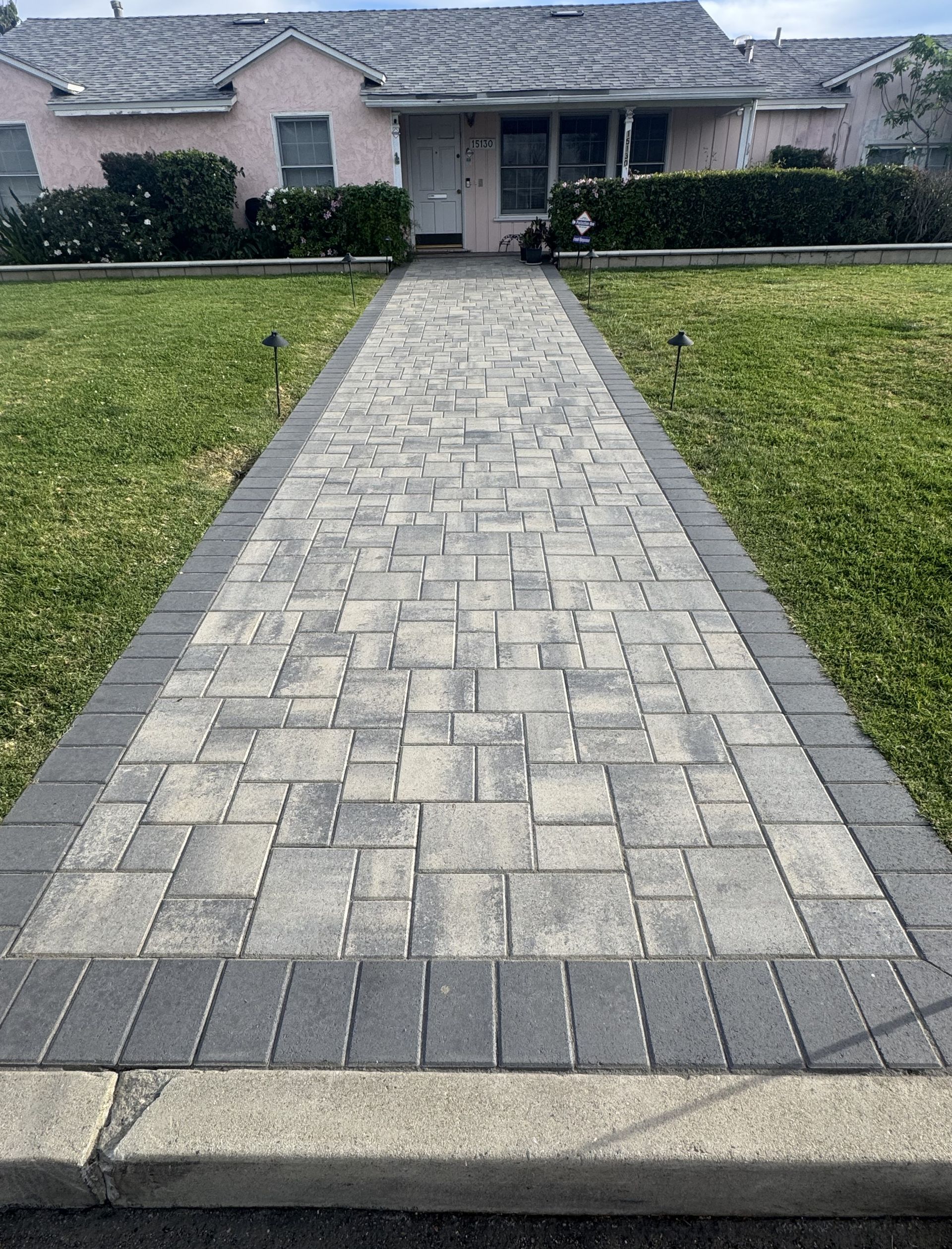Front walkway of gray stone pavers leading to a single-story house with trimmed lawn and shrubs.