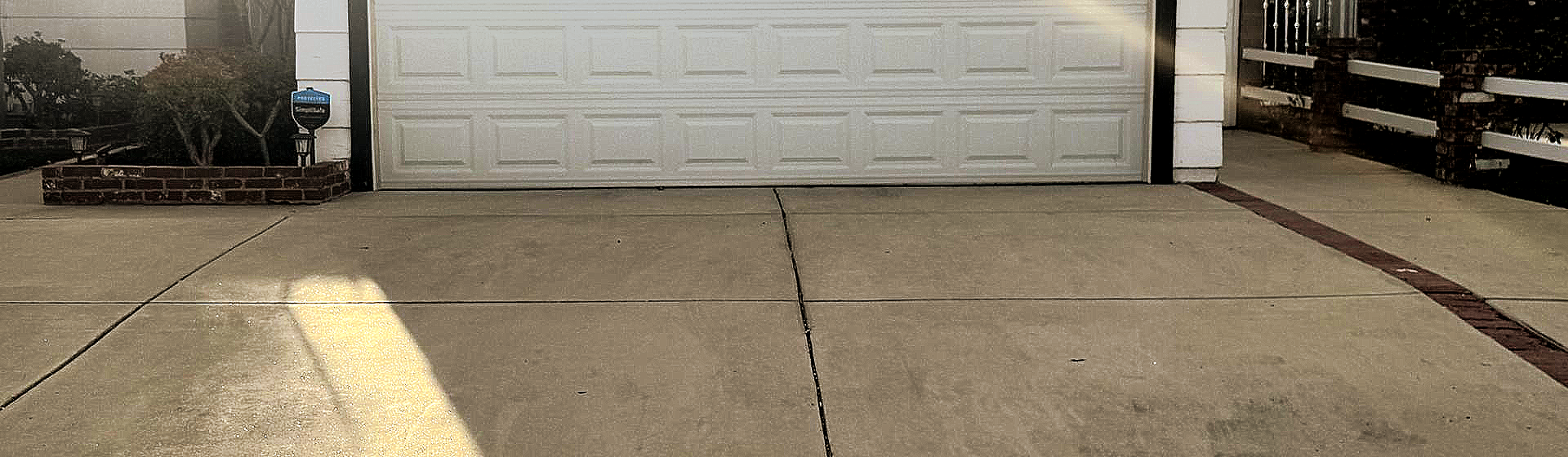 Concrete driveway leading to a white garage door with a curb and steps on the right.