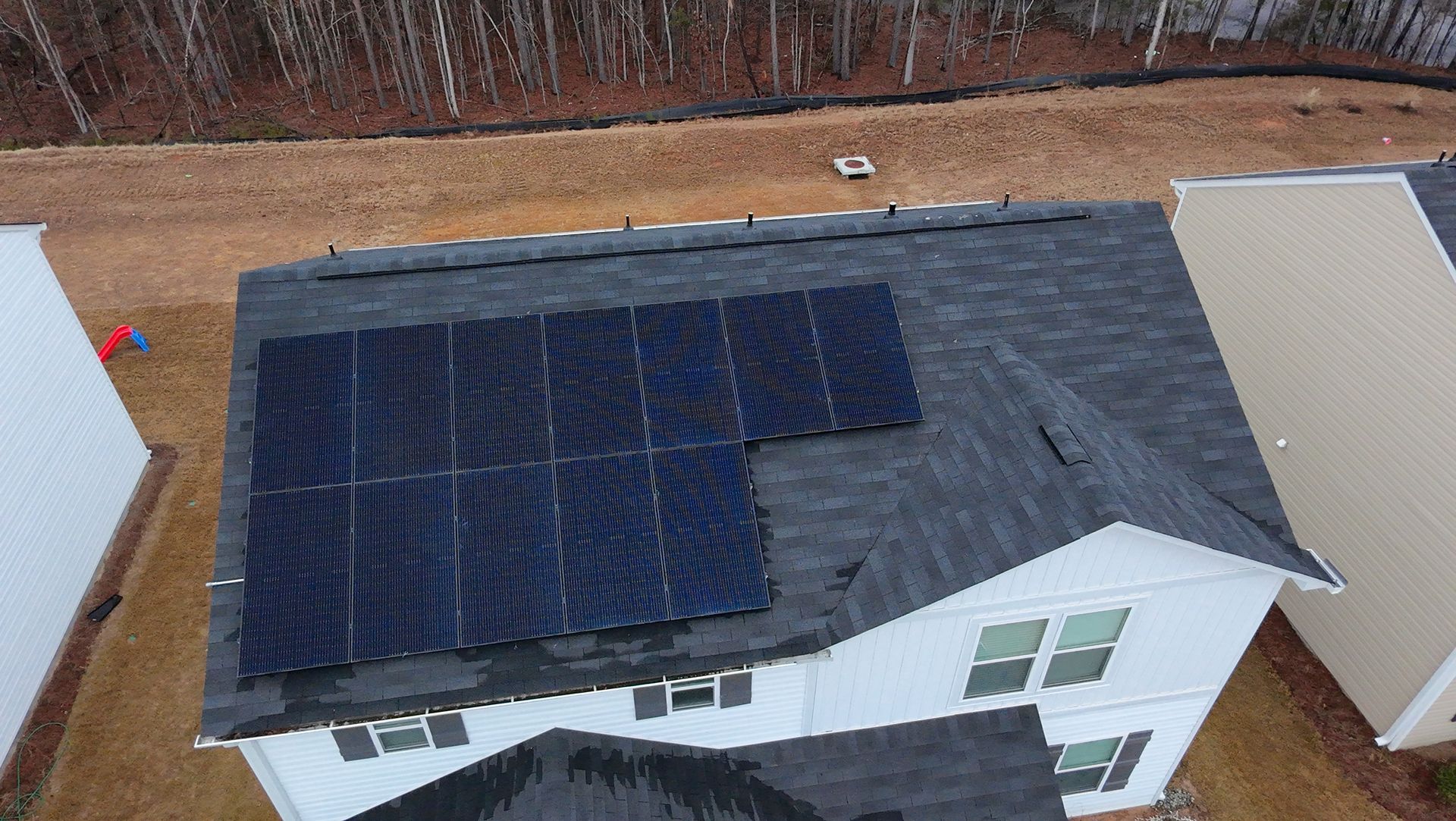 Overhead view of a house with solar panels on a dark shingled roof; exterior is white.