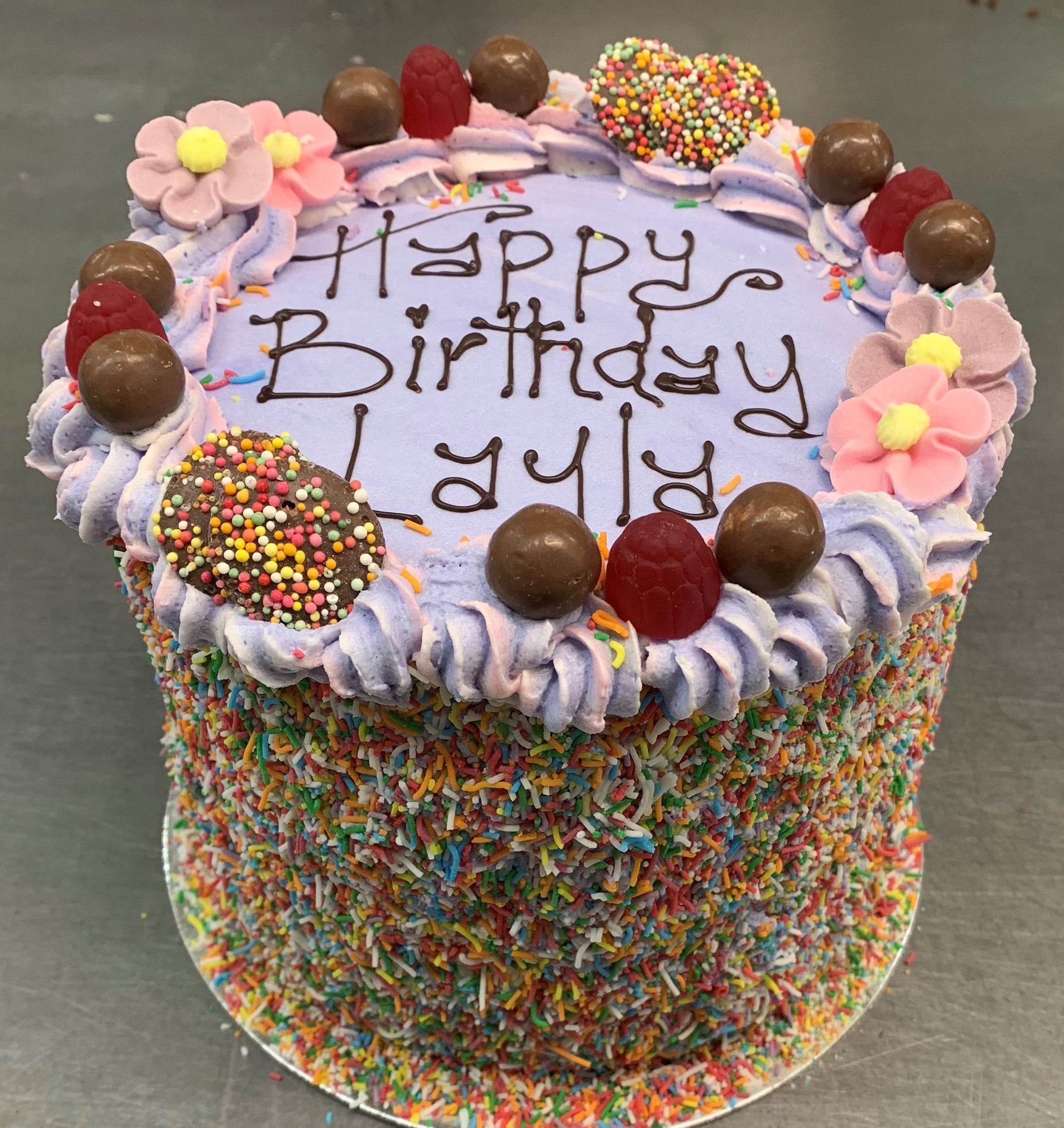 Birthday cake decorated with purple frosting, sprinkles, candies, and flowers; text reads 